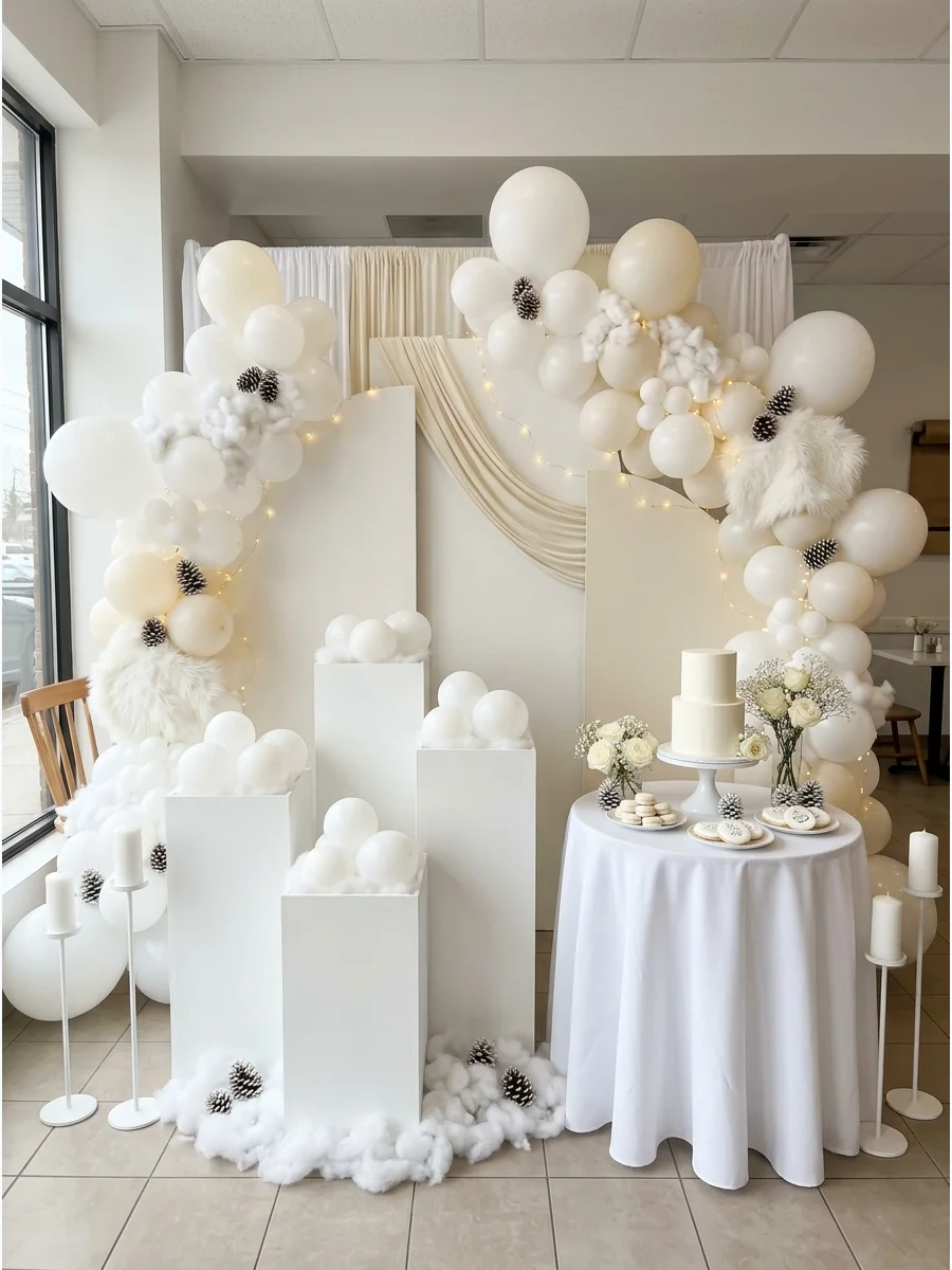An all-white baby shower decoration with balloon blocks and fabric drapes.