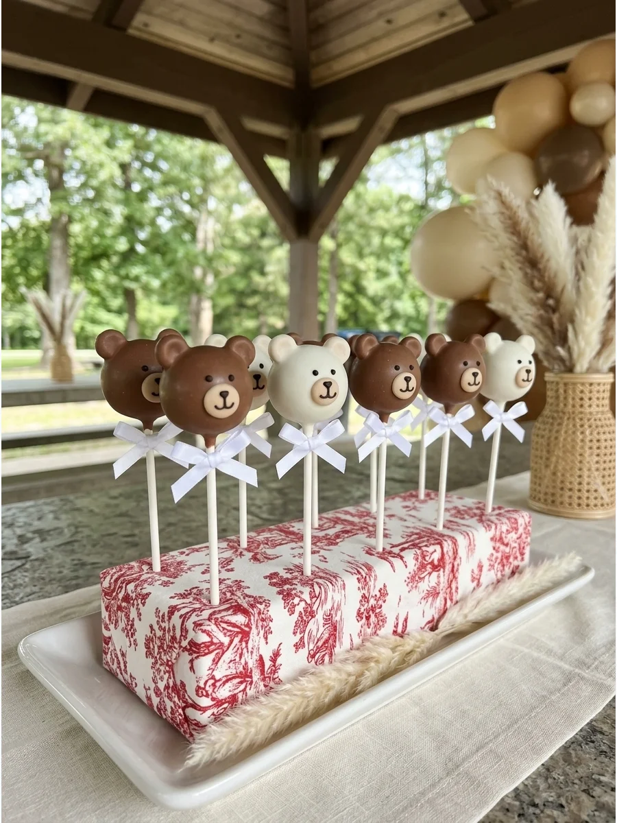 Chocolate cake pops shaped like teddy bears with small white bows on sticks.