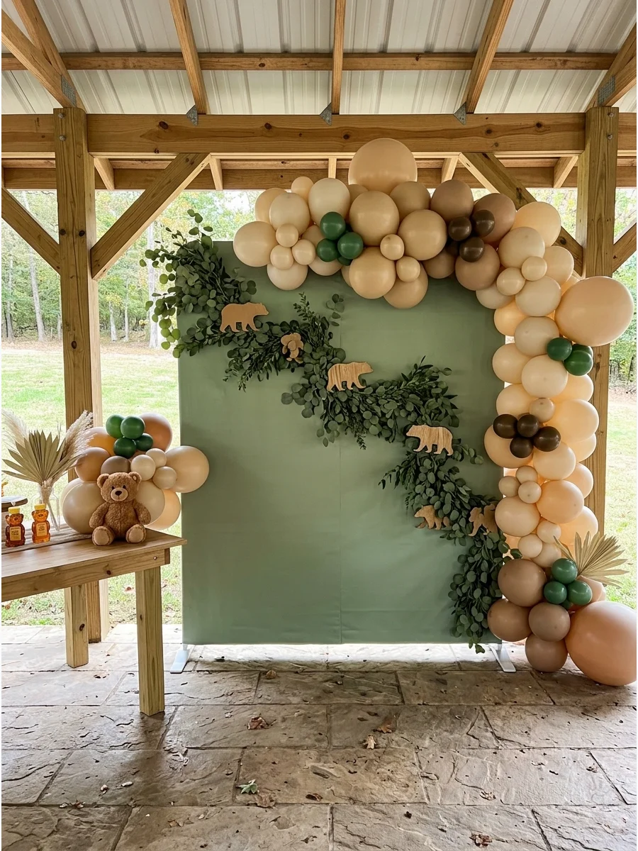 A sage green and tan backdrop with greenery and wooden bear accents.