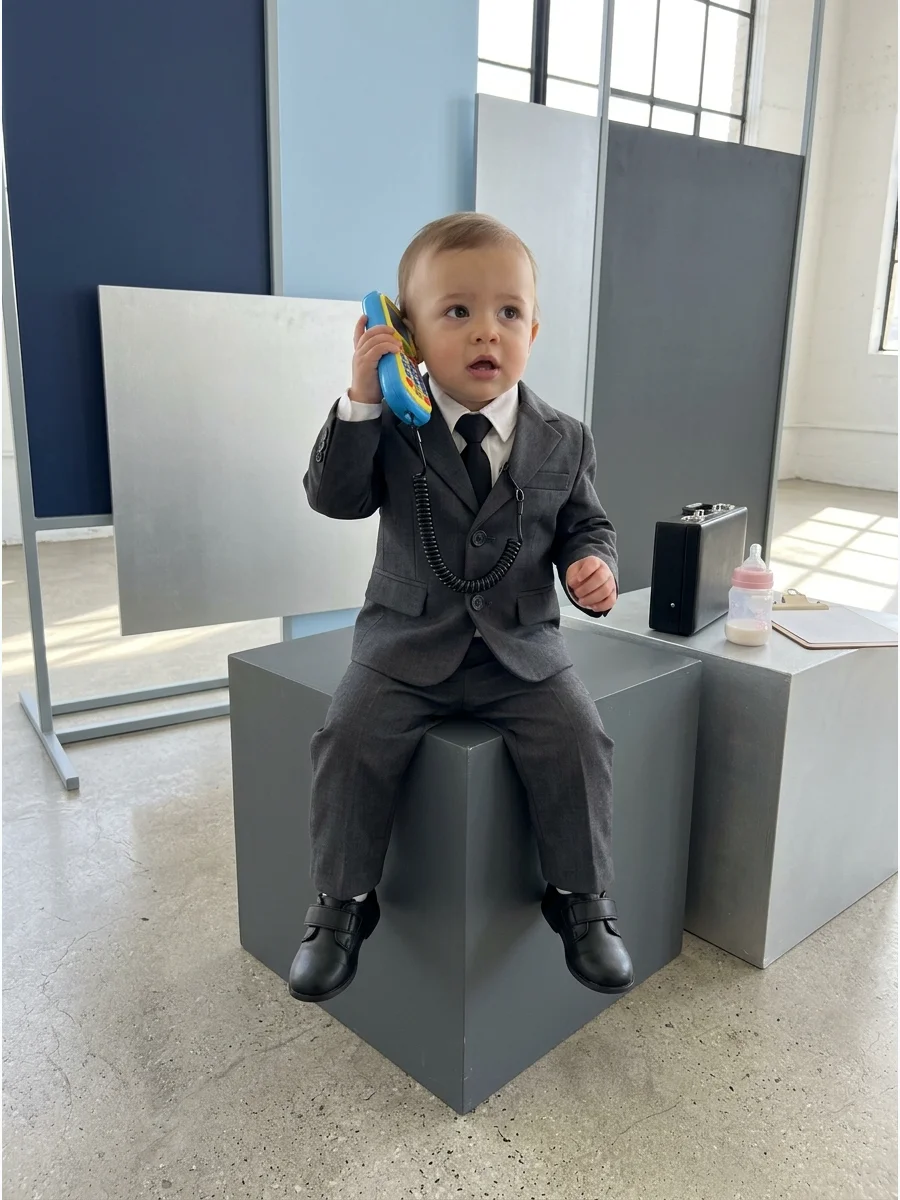 Baby in a suit pretending to talk on a toy phone.