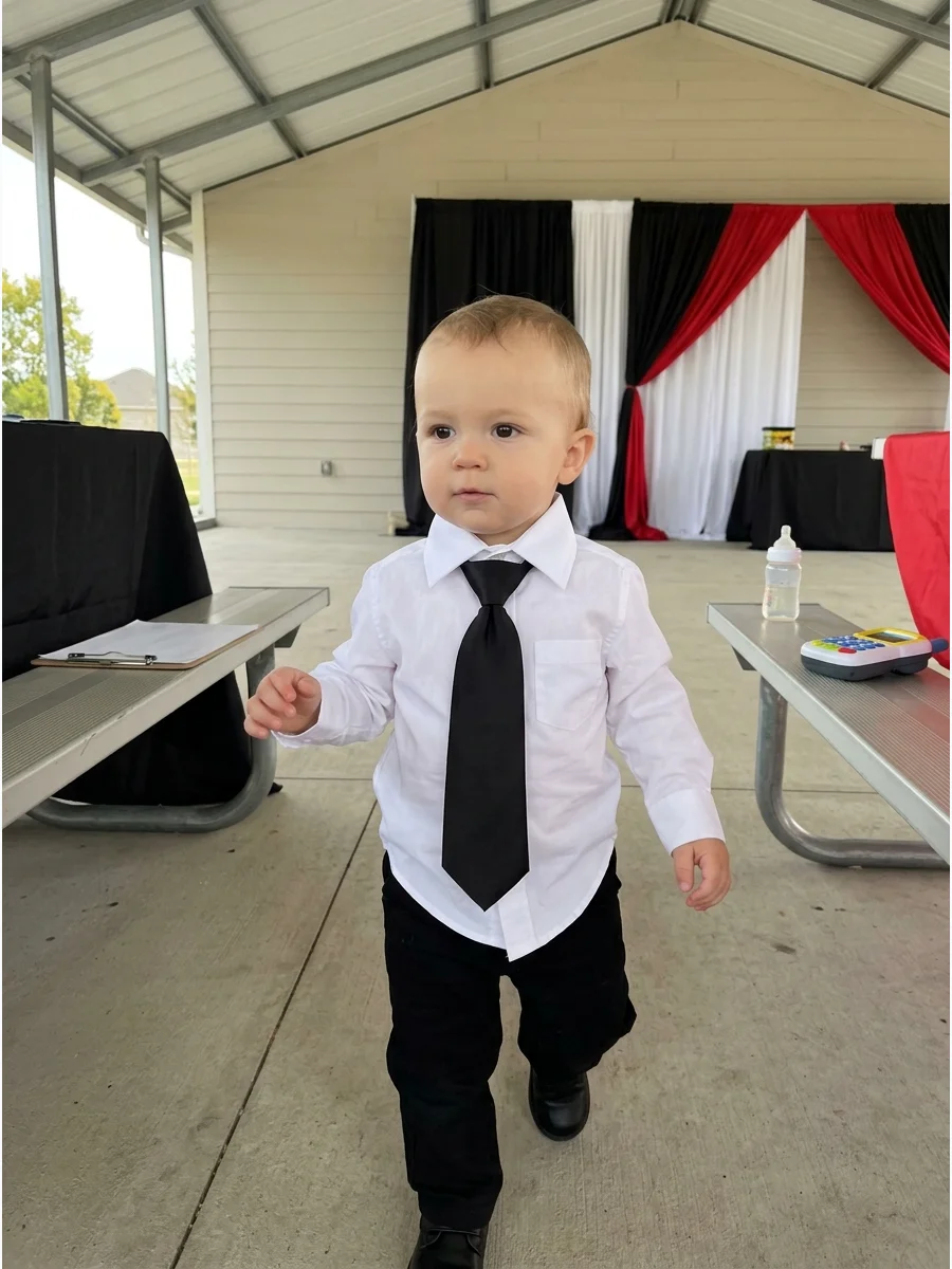 Toddler in a white shirt and long black tie.