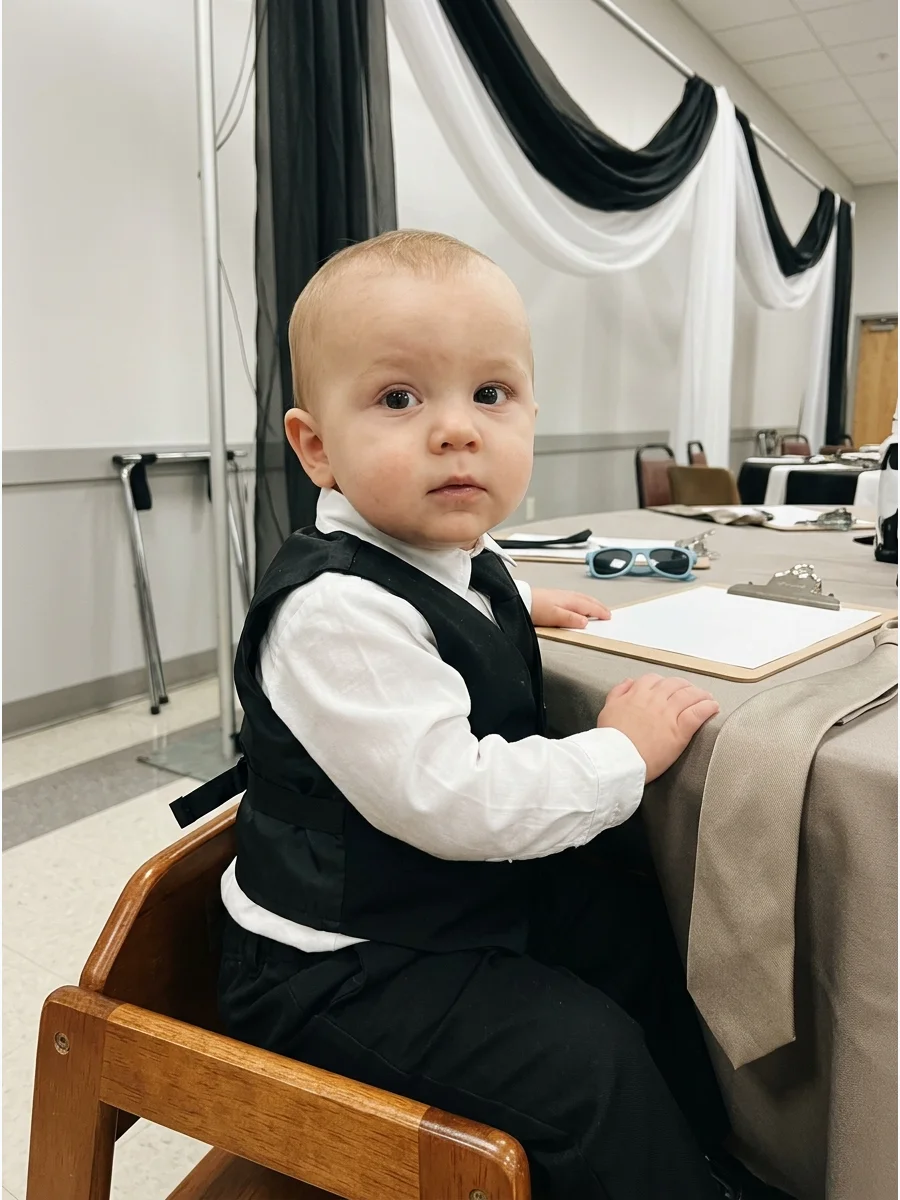 Baby wearing a black vest and white shirt.