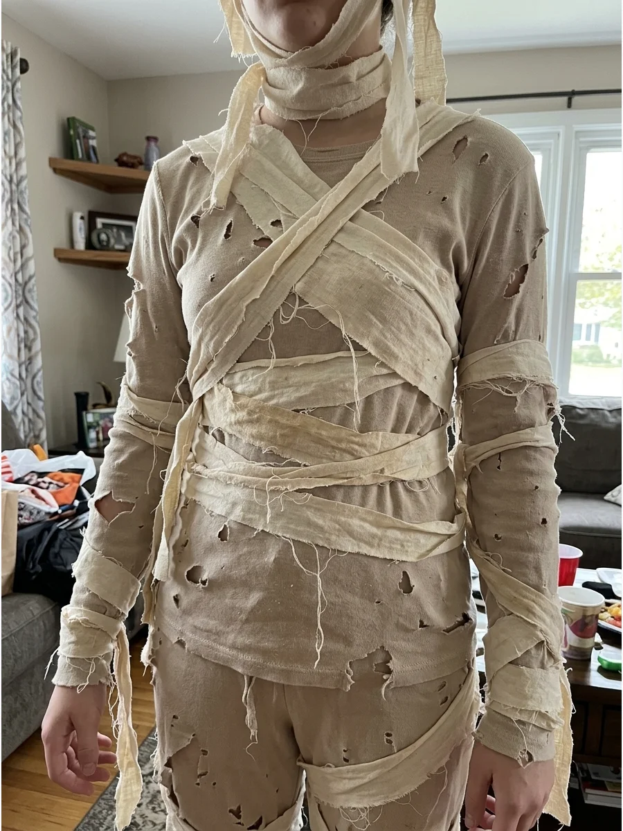 Thrifted Mummy Costume. Purchase an inexpensive white shirt and pants from a secondhand store and distress them with small tears and frayed edges. Add strips from an old sheet to c