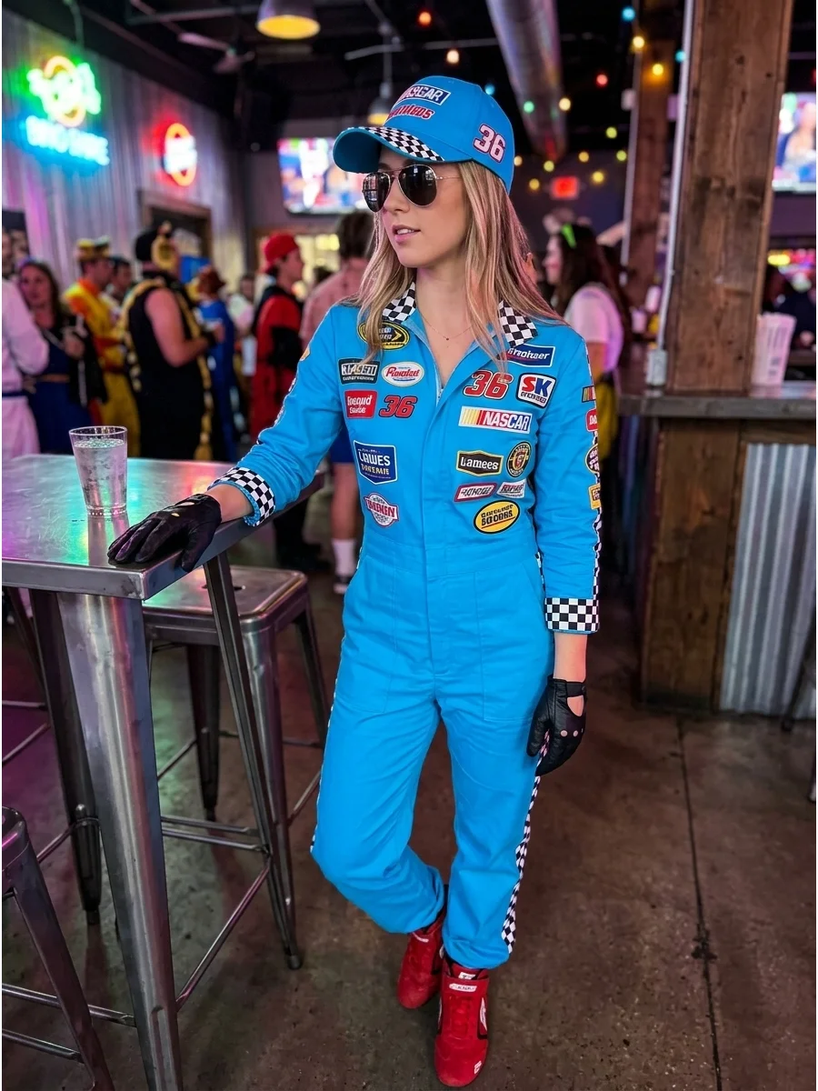 A woman in a blue NASCAR-style jumpsuit with sponsorship patches standing in a bar.