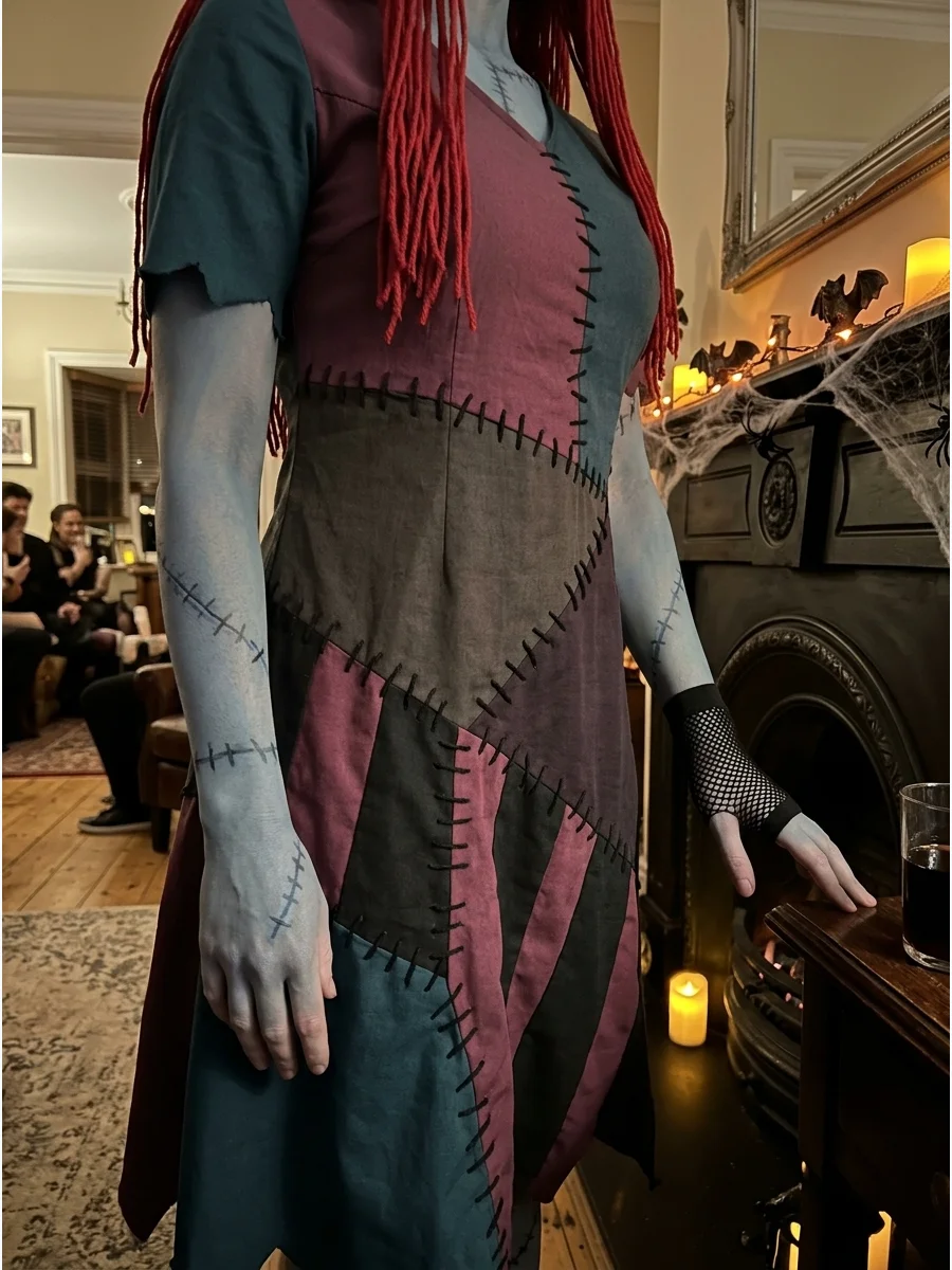 A person wearing a dark teal and plum gothic Sally dress near a fireplace.