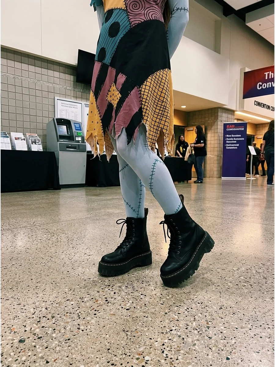 A person wearing high platform boots and a Sally patchwork dress in a lobby.