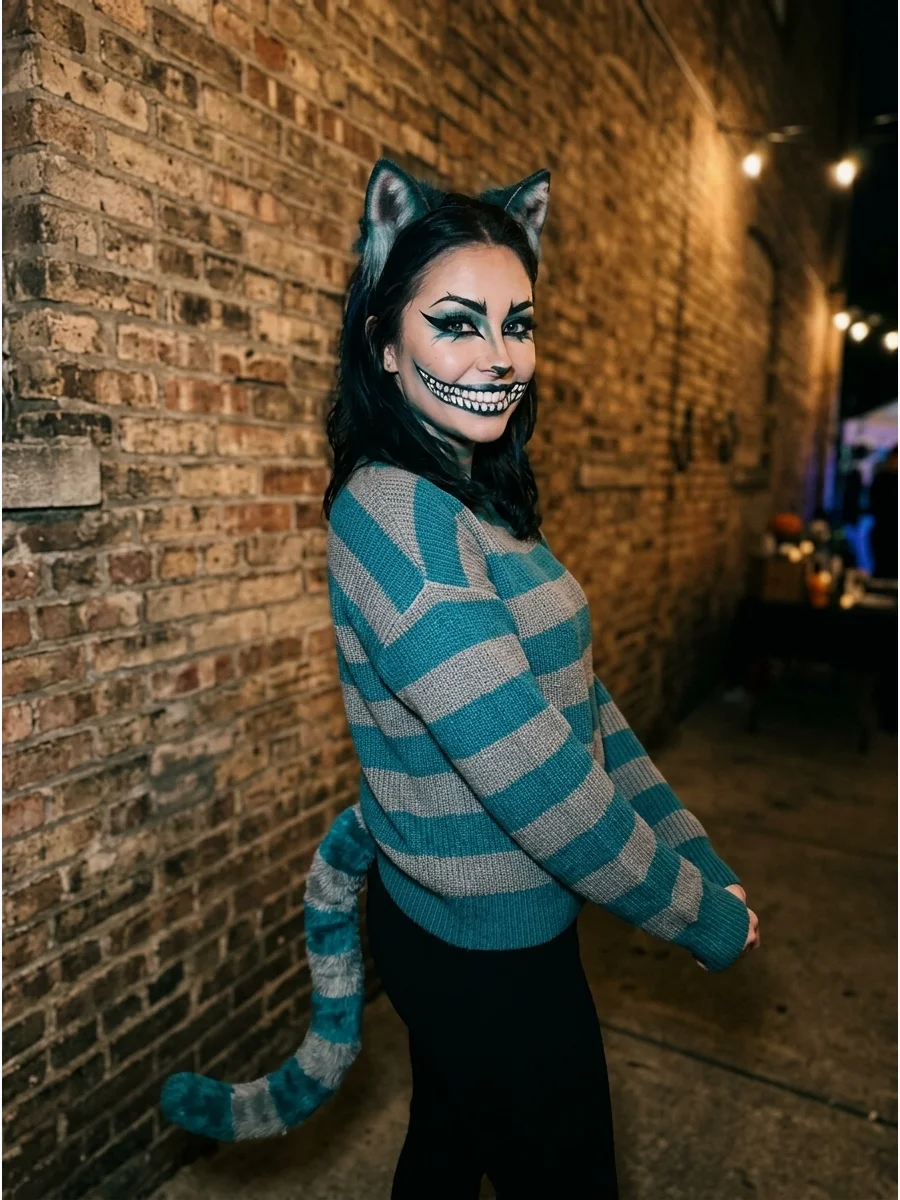 A person in a teal and gray striped Cheshire Cat costume standing against a brick wall.