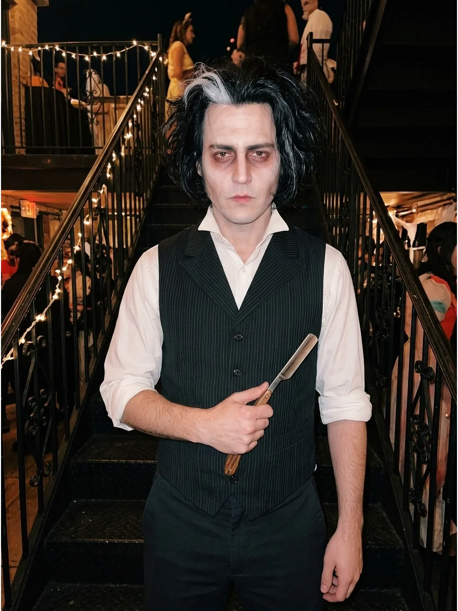A man in a Sweeney Todd costume holding a prop razor on a dark staircase.