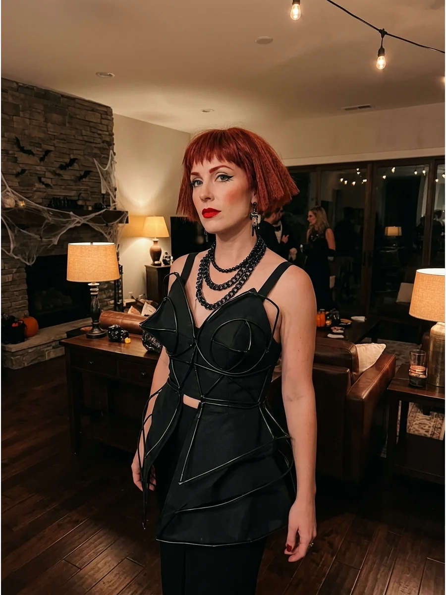 A woman in a sculptural black outfit with red hair.