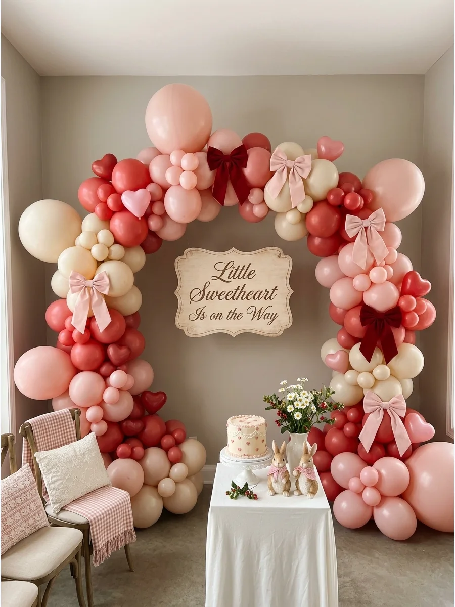 A large pink and red balloon arch with a baby shower sign in an indoor studio.