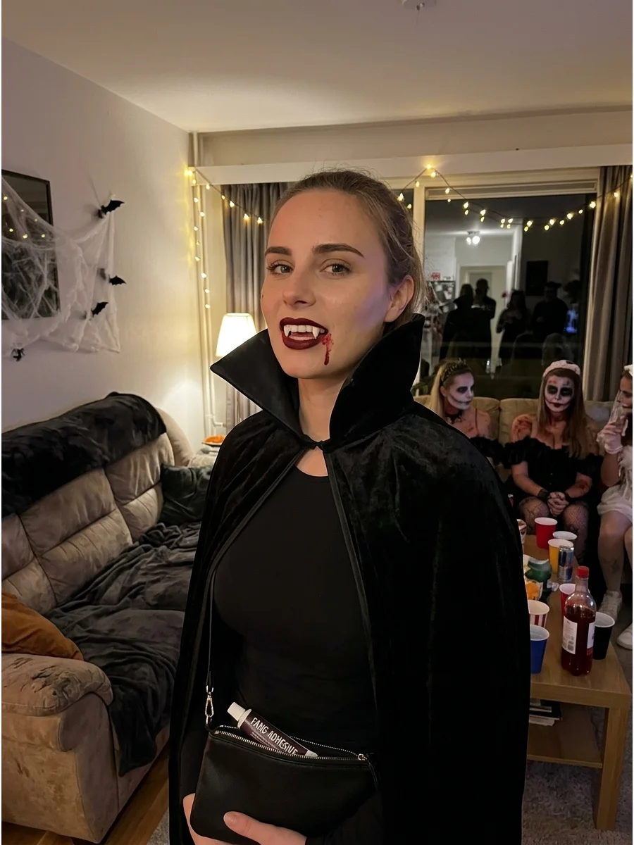 A woman in an all-black outfit with a vampire cape and fangs.