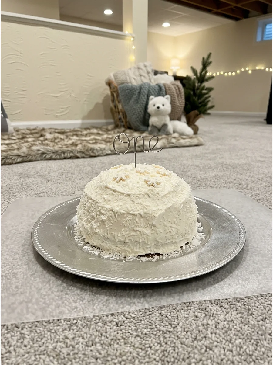 A round snowball-themed smash cake with white frosting and silver accents.