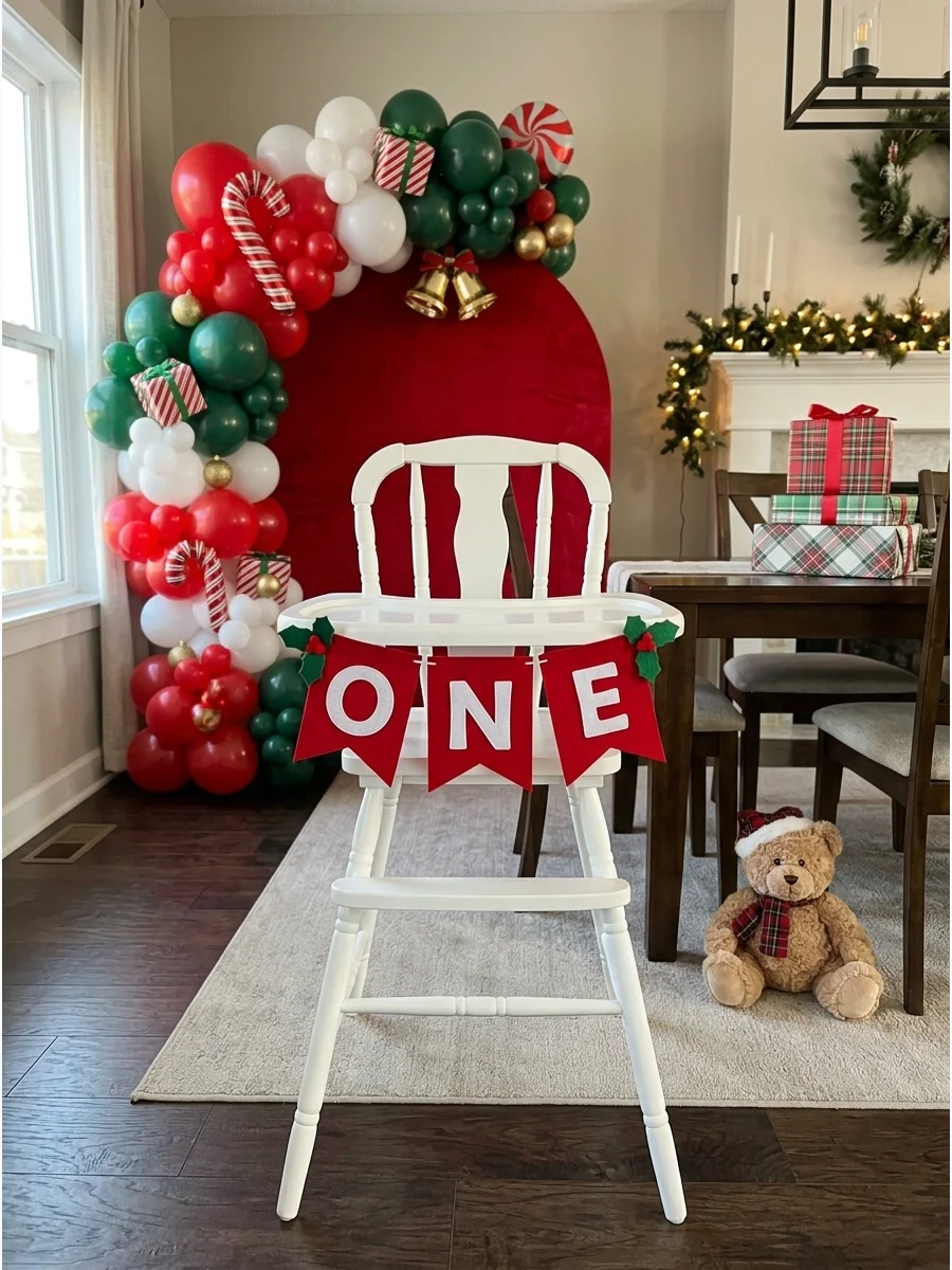 A baby high chair decorated with a holly leaf ONE banner for a Christmas birthday.