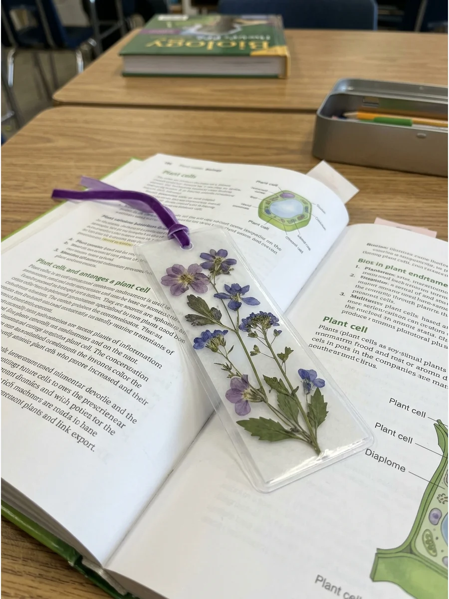 A transparent bookmark featuring pressed purple flowers and a ribbon.
